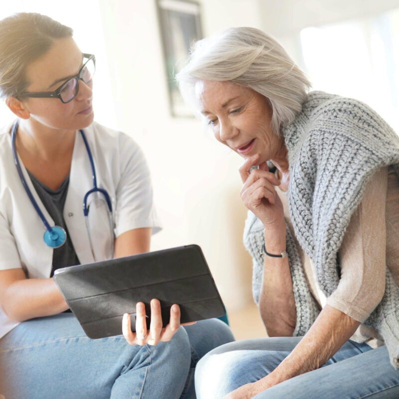 Compassionate doctor attentively explains health information on a tablet to an older woman, creating a supportive moment.